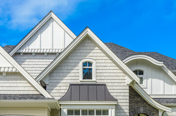 Top of grey stucco luxury house with shingle roof, red and yellow trees and nice windows in Summer in Vancouver, Canada, North America. Day time on June 2024.