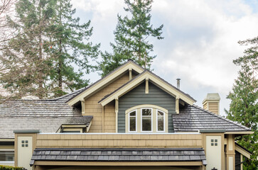 Top of grey stucco luxury house with shingle roof, red and yellow trees and nice windows in Summer in Vancouver, Canada, North America. Day time on June 2024.
