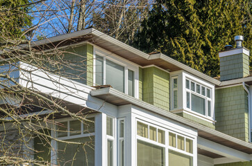 Top of grey stucco luxury house with shingle roof, red and yellow trees and nice windows in Summer in Vancouver, Canada, North America. Day time on June 2024.