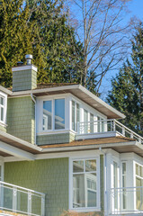 Top of grey stucco luxury house with shingle roof, red and yellow trees and nice windows in Summer in Vancouver, Canada, North America. Day time on June 2024.