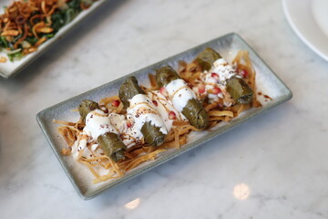  A plate of Mediterranean stuffed grape leaves topped with yogurt and pomegranate seeds, elegantly presented on a marble table.
