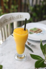Refreshing mango smoothie served in a tall glass with a straw, capturing the vibrant yellow color and tropical essence on a marble table.