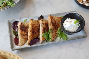 A plate of Lebanese arais, grilled flatbread stuffed with savory chicken filling, served alongside a creamy labneh dip and fresh greens, offering a delicious Middle Eastern appetizer.