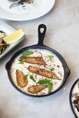 A skillet of Lebanese eggplant fatteh, layered with fried eggplant, creamy yogurt sauce, toasted bread, chickpeas, and garnished with fresh mint and sumac, showcasing a traditional and flavorful Middl