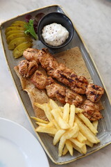 Grilled chicken skewers served with crispy fries, creamy garlic sauce, pickles, and fresh greens on a rectangular plate for a delightful meal.