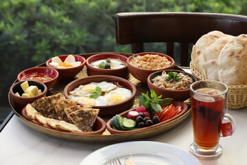 A traditional Lebanese breakfast spread featuring fried eggs, zaatar, hummus, labneh, butter, apricot jam, fresh vegetables, olives, and Lebanese bread, beautifully arranged on a rustic tray.