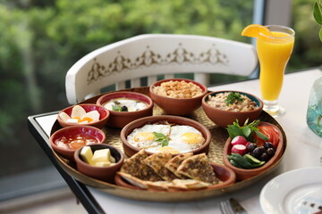 A traditional Lebanese breakfast spread featuring fried eggs, zaatar, hummus, labneh, butter, apricot jam, fresh vegetables, olives, and Lebanese bread, beautifully arranged on a rustic tray.