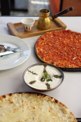 A traditional Lebanese breakfast spread featuring tomato manoushe, cheese manoushe, and a bowl of creamy labneh garnished with an olive and dried herbs, served on a rustic setup.