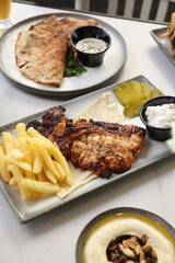 A Lebanese platter featuring tender grilled chicken, crispy French fries, tangy pickles, and creamy garlic sauce, beautifully served on flatbread with a rustic presentation.