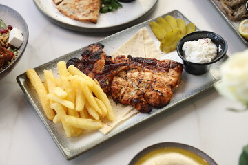 A Lebanese platter featuring tender grilled chicken, crispy French fries, tangy pickles, and creamy...