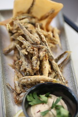 A platter of crispy fried fish served with a creamy tahini dip garnished with fresh parsley and a lemon wedge, offering a flavorful and traditional Lebanese seafood appetizer.