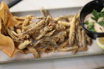 A platter of crispy fried fish served with a creamy tahini dip garnished with fresh parsley and a lemon wedge, offering a flavorful and traditional Lebanese seafood appetizer.