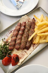 A platter of chargrilled Lebanese beef kebabs served with crispy French fries, grilled tomatoes, onions, fresh parsley, and sumac seasoning on flatbread, offering a hearty and flavorful Middle Eastern