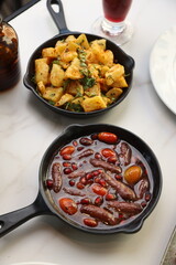 Makanek Lebanese sausages served in a black skillet with pomegranate seeds and cherry tomatoes, offering a vibrant and flavorful presentation.