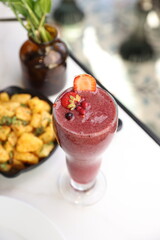 A vibrant berry smoothie topped with fresh strawberry and pomegranate garnish, served on a light table setup with a gourmet touch.