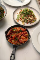 A skillet of Lebanese makanek sausages cooked with sautéed onions, tomatoes, and garlic in a rich, tangy tomato-based sauce, garnished with fresh parsley.