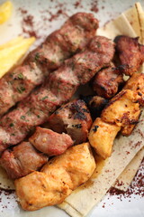 A Lebanese mixed grill platter featuring chargrilled beef kebabs, chicken skewers, and lamb skewers, served with French fries, garlic sauce, grilled tomatoes, fresh parsley, and sumac on flatbread, of
