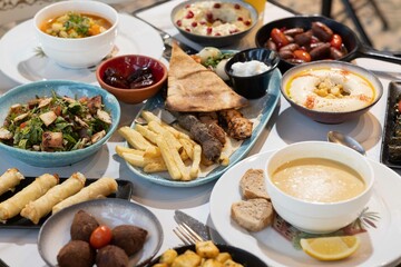 A vibrant Lebanese breakfast feast featuring mixed grill, hummus with pomegranate garnish, fattoush, lentil soup, kibbeh, fried potatoes, cheese rolls, garlic sauce, and fresh salad, served with flatb