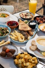 A vibrant Lebanese breakfast feast featuring mixed grill, hummus with pomegranate garnish, fattoush, lentil soup, kibbeh, fried potatoes, cheese rolls, garlic sauce, and fresh salad, served with flatb