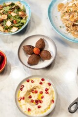  A vibrant display of Middle Eastern mezze featuring kibbeh, creamy hummus with pomegranate seeds, and yogurt dip. A delicious cultural culinary experience.