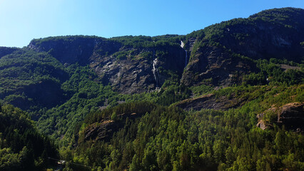Obraz premium Majestic Mountain Landscape with Dense Forests and Cascading Waterfalls Under a Clear Blue Sky