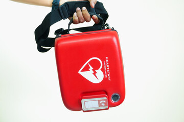 Male hand holding AED or defibrillator Red machine on white background. First Responder Holding Portable Defibrillator