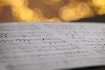 Sheet of musical notes against blurred lights, closeup. Bokeh effect