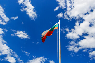 Bulgarian national flag on a metal pole against sunny sky with clouds