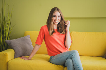 Obraz premium Photo of lovely young girl sit sofa touch hair dressed orange garment spacious house spring indoors room