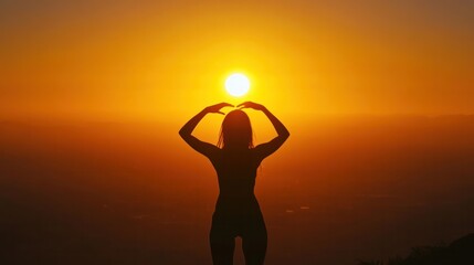 A woman standing on a hilltop during sunrise, forming a frame with her hands around the bright sun emerging from the horizon