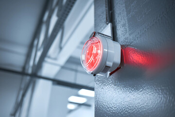 Fire alarm evacuation monitoring concept. A red alarm light mounted on a wall, indicating an alert or emergency situation in a modern industrial setting.