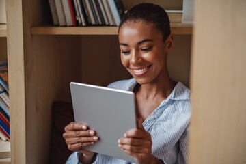 Naklejka premium Smiling Young African Woman Using Tablet Cozy Home Office Setting