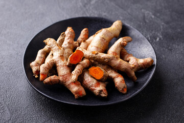 Fresh turmeric, curcumin roots on a black plate. Superfood product. Dark background. Close up.