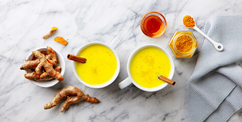 Turmeric tea, latte, golden milk in cups with cinnamon and fresh roots turmeric. Marble background. Top view.