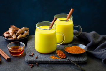 Turmeric latte, tea, golden milk in glass mugs with cinnamon. Grey background. Close up.