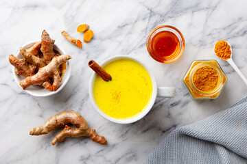 Turmeric latte, tea, golden milk in cups with cinnamon. Marble background. Close up. Top view.