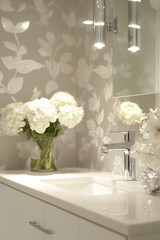 Modern bathroom with a floral-patterned wallpaper, white hydrangeas in a glass vase, and a sleek sink, creating a serene and stylish interior design scene