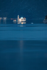 Obraz premium Scenic view of Our lady of the rocks island church glowing in the bay of Kotor, Montenegro at twilight with mountains in the background