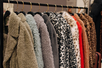 Different fur coats, winter outerwear hanging in a row on hangers in a fashion luxury boutique