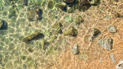 Cenital aerial view of clean transparent sea water, sand and rocks on the beach on sunny day