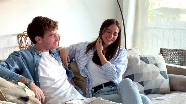 Sitting together on the sofa, a couple is smiling and talking about their free time activities, planning future vacations, and discussing how they can balance work and personal life to make more time 