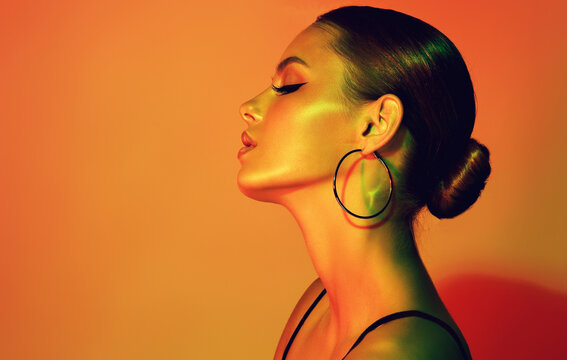 Fashion model woman in colorful bright lights with trendy makeup . Beautiful girl with earrings jewelry Beauty and accessories. Neon and orange with green color