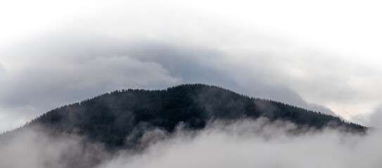 Panorama of a mountain foothill surrounded by mist and clouds fading to transparent at the top
