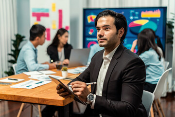Portrait of businessman or analyst looking at camera with his colleague analyzing data analysis in dynamic business strategy investment planning meeting. Meticulous