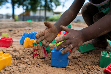 Manos de un niño de color jugando con tierra y cubos de colores. Generado con IA