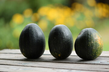 Ornamental dark green pumpkins on wooden table, bokeh background with yellow blooming flowers, autumn background with pumpkins, selective focus, blurred background, space for text.