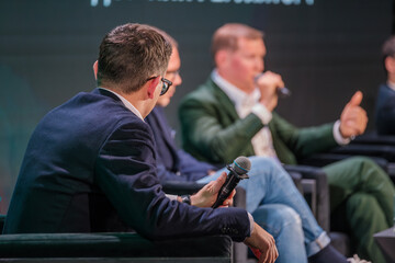 Corporate leaders engaging in discussion on stage with microphones and audience. Professional conversation during formal event.