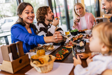 Family and friends gathered in a restaurant to eat delicious food, talk, drink and hang out.