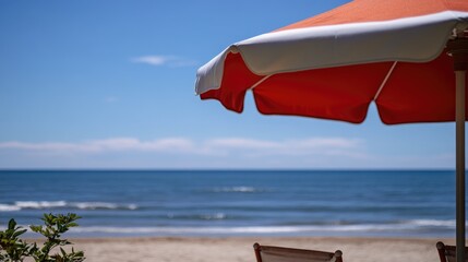 Vibrant red and white sun umbrella overlooking a serene beach with gently lapping ocean waves under a clear blue sky.