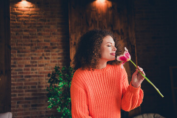 Photo of pretty young woman closed eyes smell flower wear orange pullover loft interior apartment...